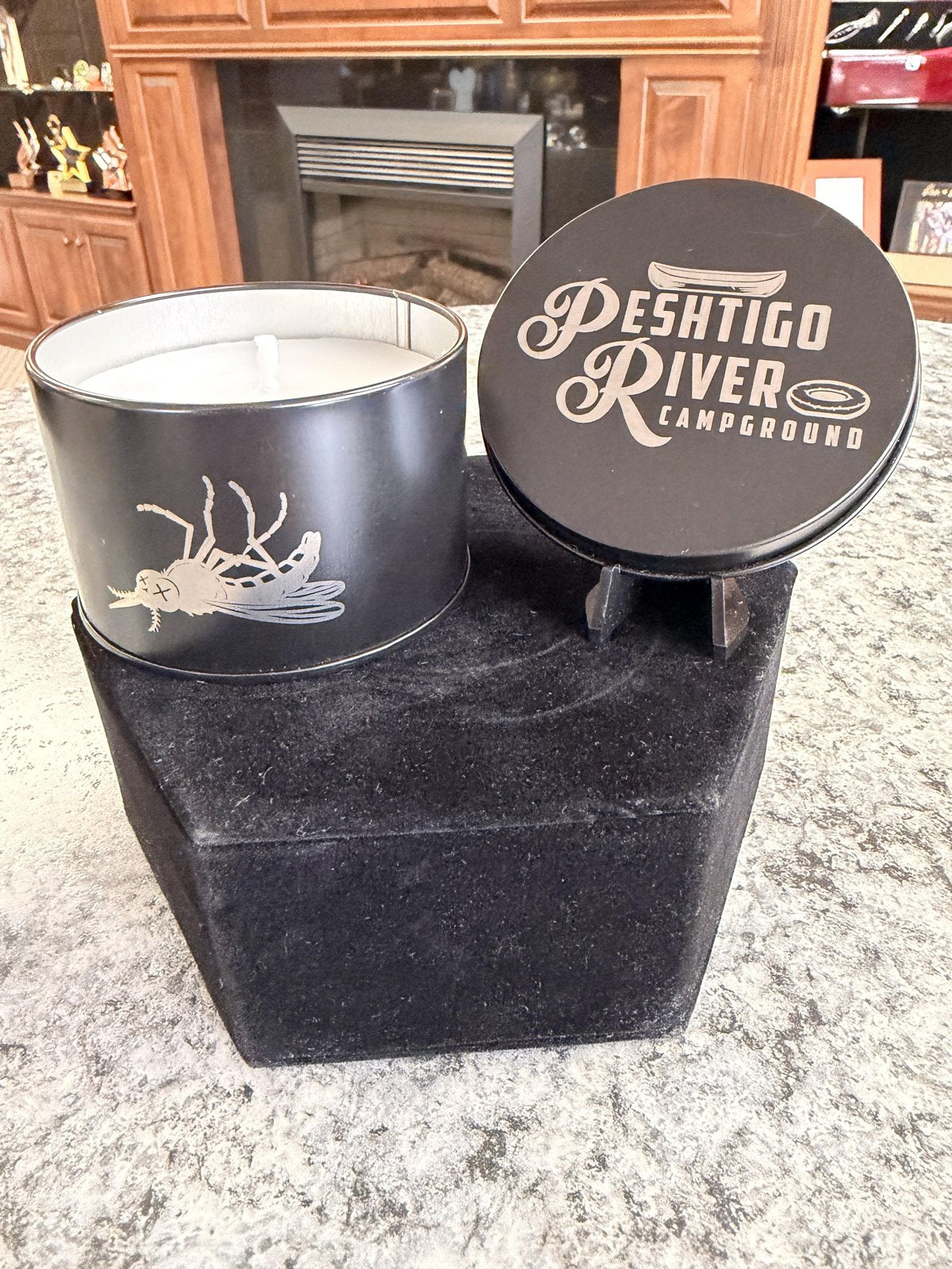 Candle with an engraved wildlife design beside a Peshtigo River Campground branded lid