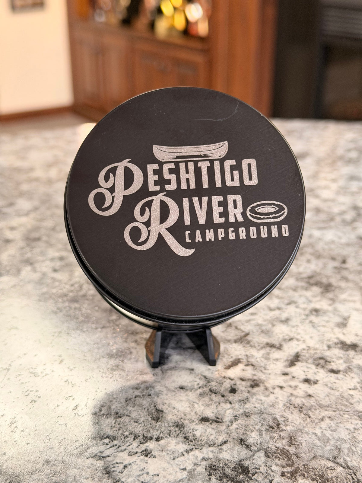 Close-up of a laser-engraved logo on a black candle tin lid