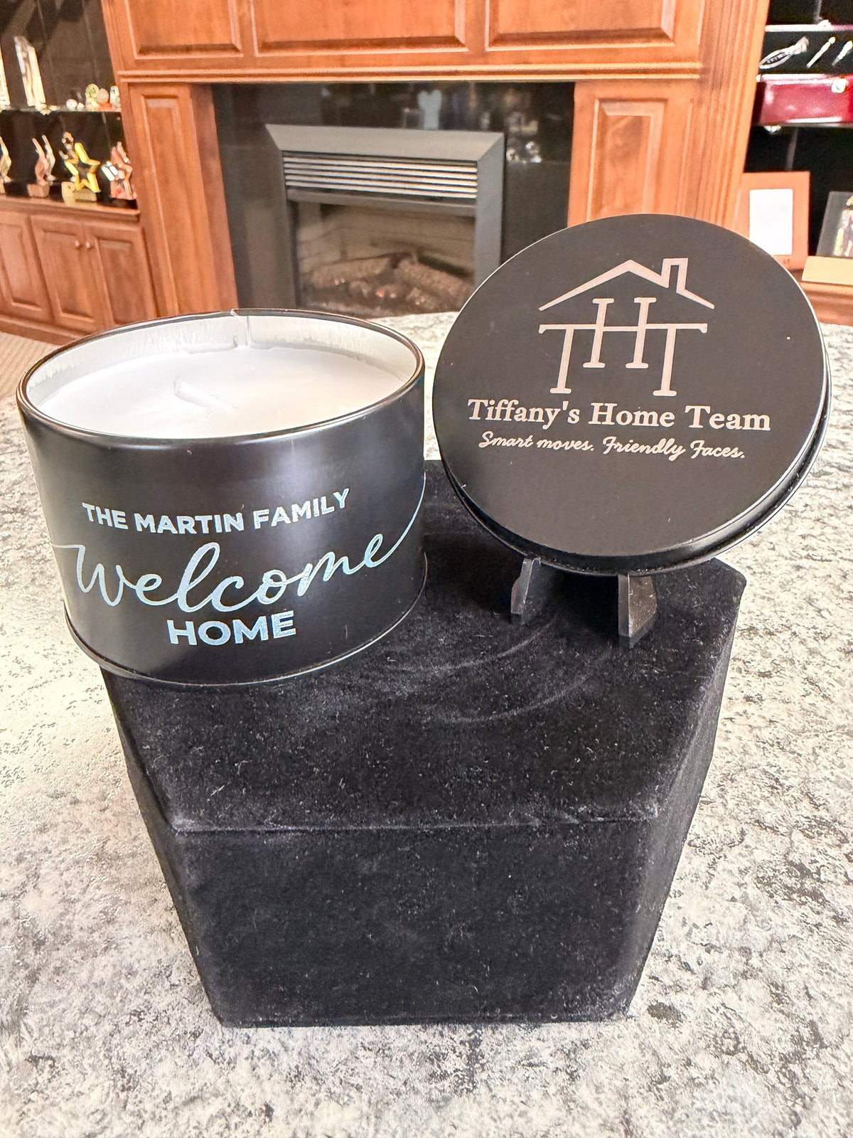 Open black tin candle with full-color side imprint and engraved house-logo lid on a stand