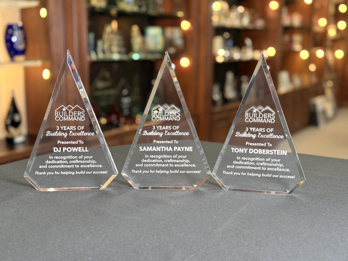 Three clear acrylic peak awards engraved with the Builders Command logo and 3 Years of Building Excellence