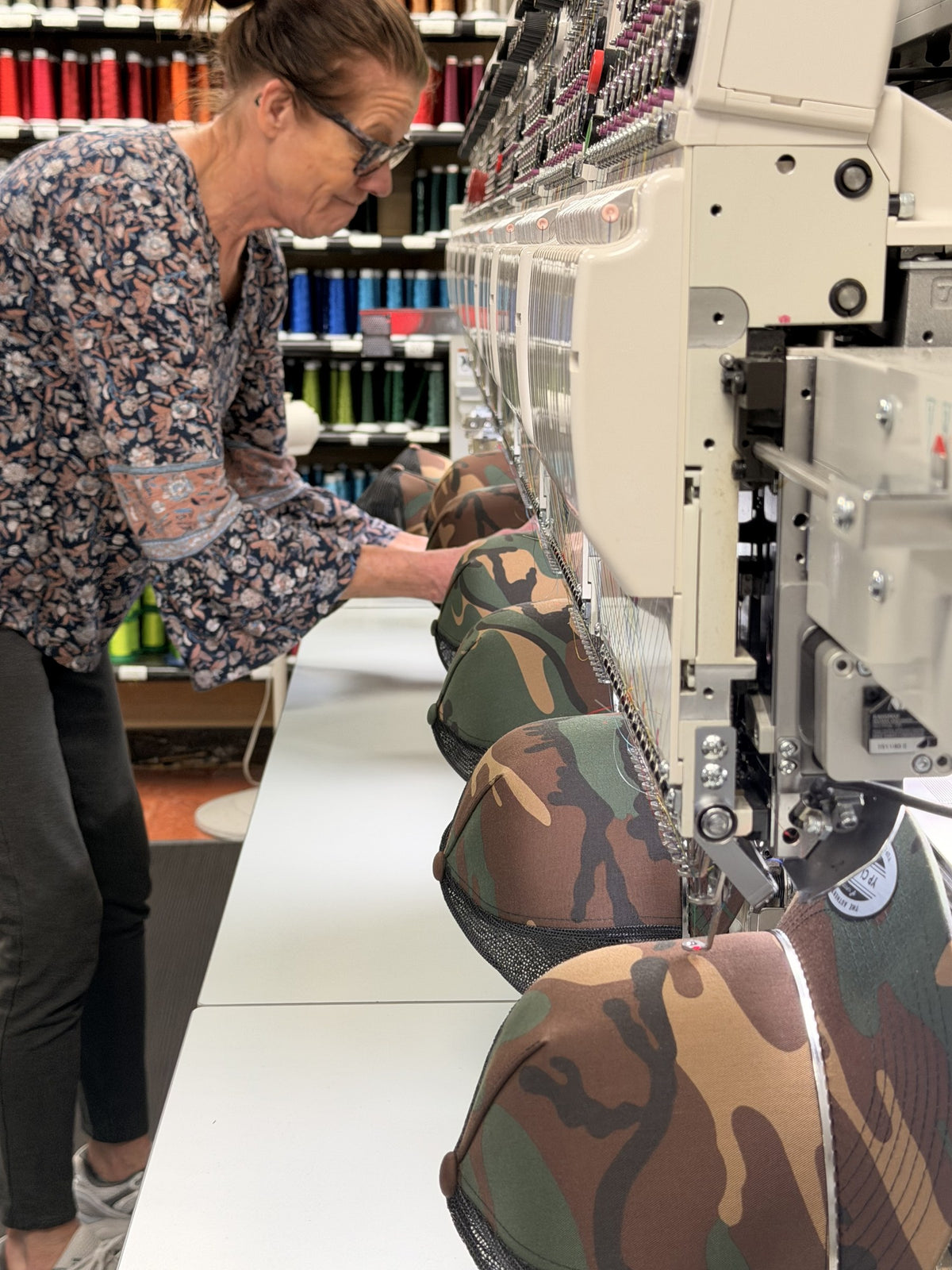 Team member working along a row of camo hats on a multi-head embroidery machine in our Green Bay shop