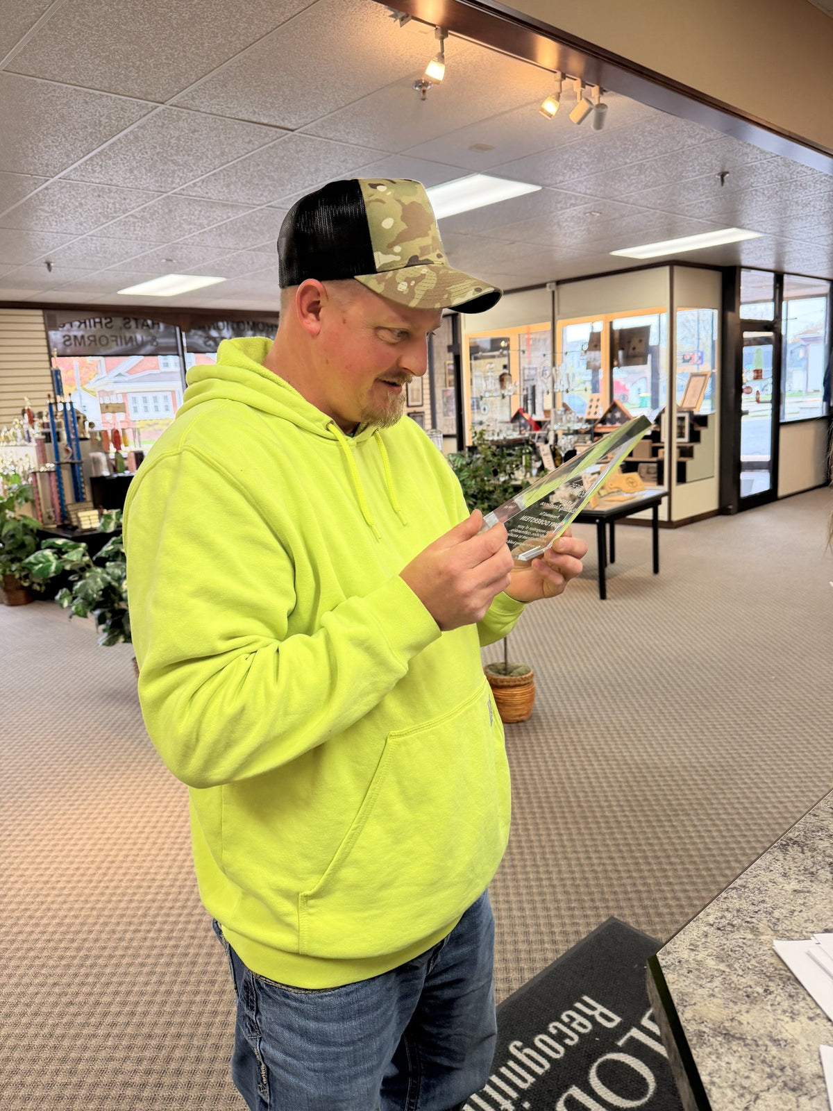 Josh, owner of Builders Command, looking over one of his team's engraved awards in our Green Bay showroom, wearing one of the camo hats we embroidered